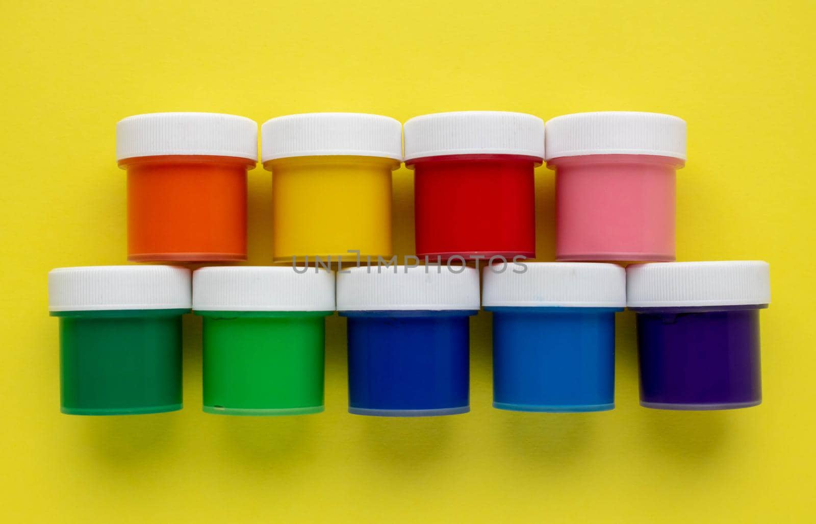 A set of colorful gouache cans isolated on a yellow background. Banks of different colors of gouache paints. by lapushka62