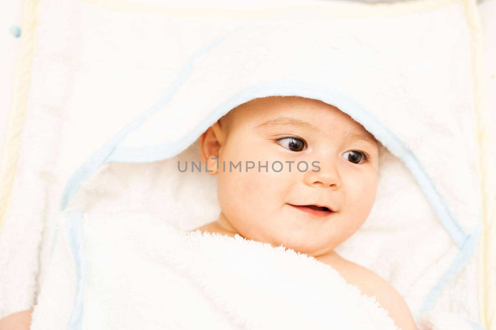 Baby boy wearing diaper and blue towel in white sunny bedroom. Newborn child relaxing in bed after bath or shower. Nursery for children. Textile and bedding for kids. New born kid with toy bear. by Mareno