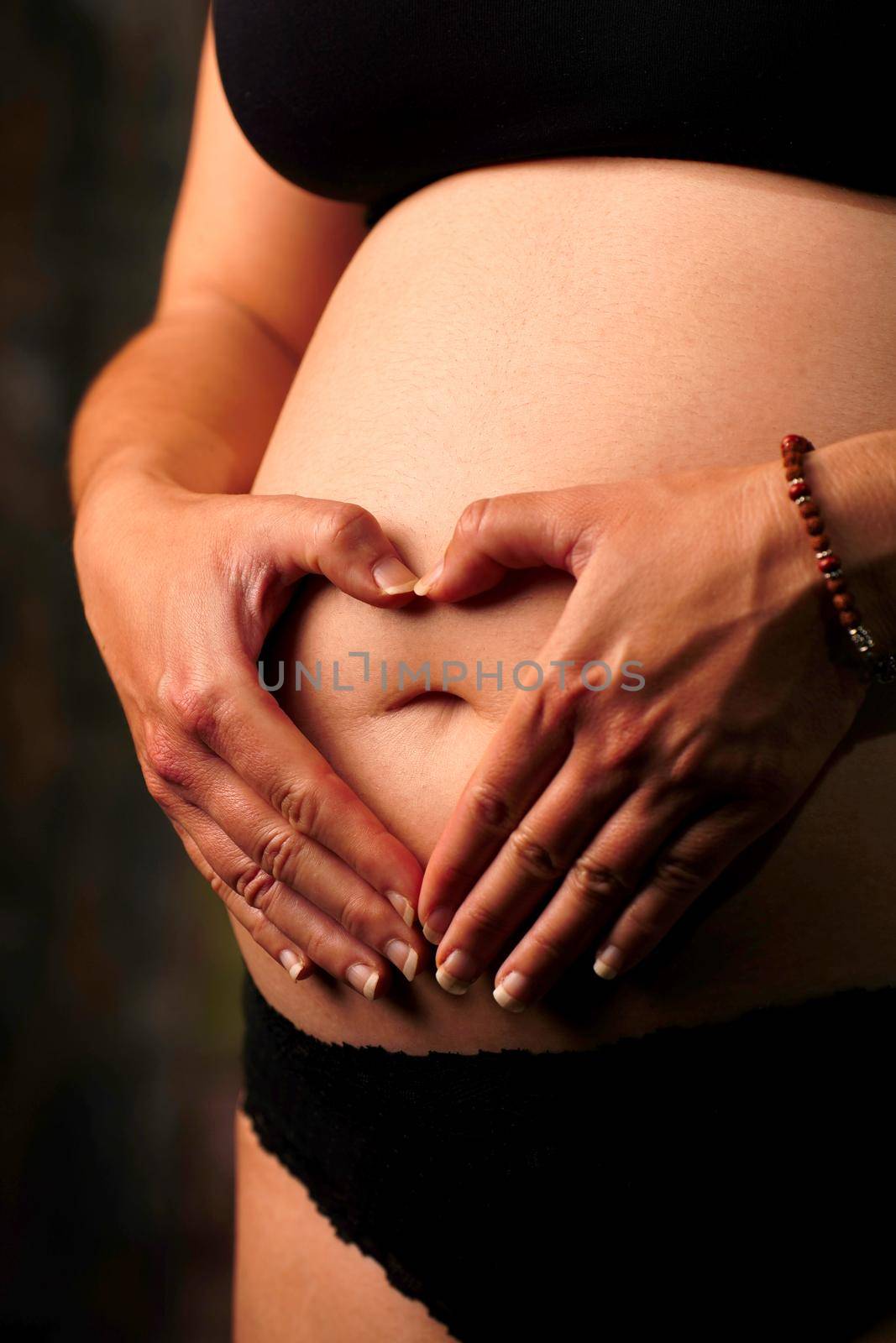 Close up of pregnant woman holding hands with heart shaped in garden by Mareno