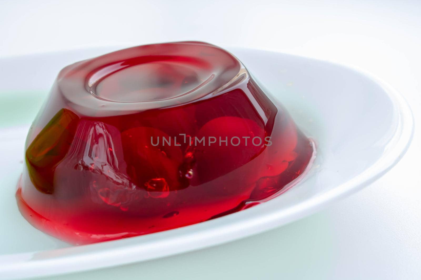 White plate with cherry berries in red jelly on a white background.