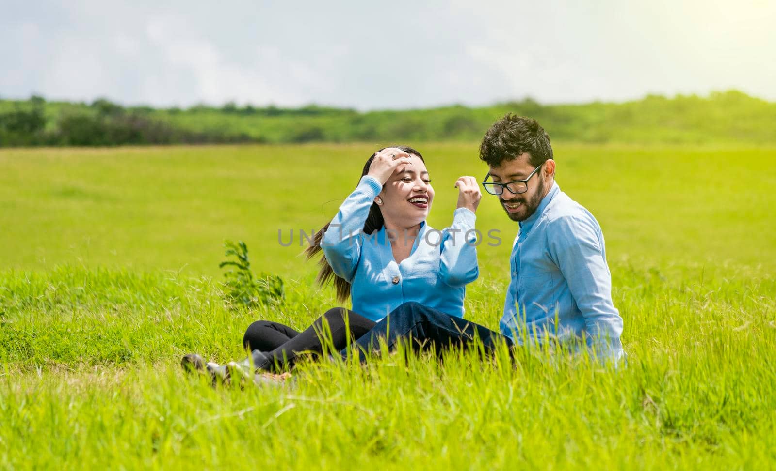 A couple in love sitting in the field, Romantic couple sitting on the grass outdoors, Smiling teenage couple sitting on the grass on a sunny day