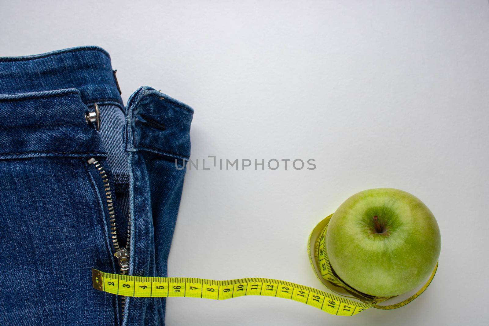 Blue jeans, a green Apple and a centimeter on a white background.Weight loss and the concept of weight loss