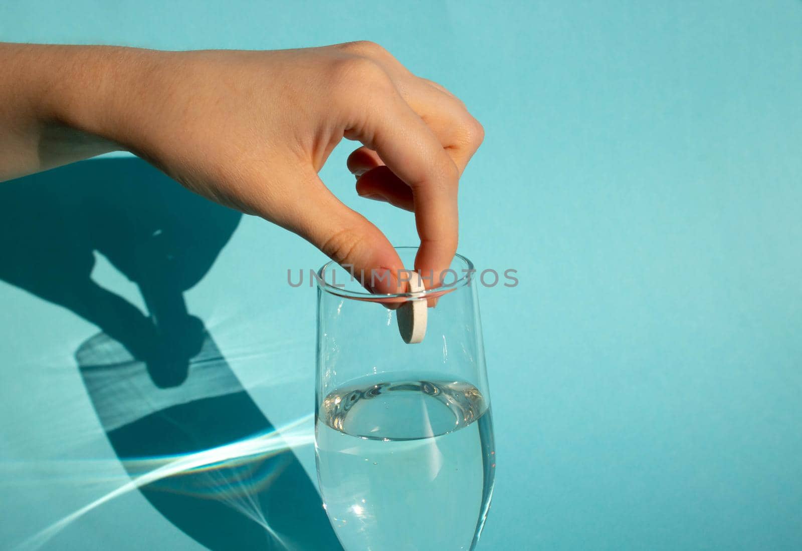 Against a blue background, a hand drops a dissolving fizzy aspirin tablet into a glass of water by lapushka62