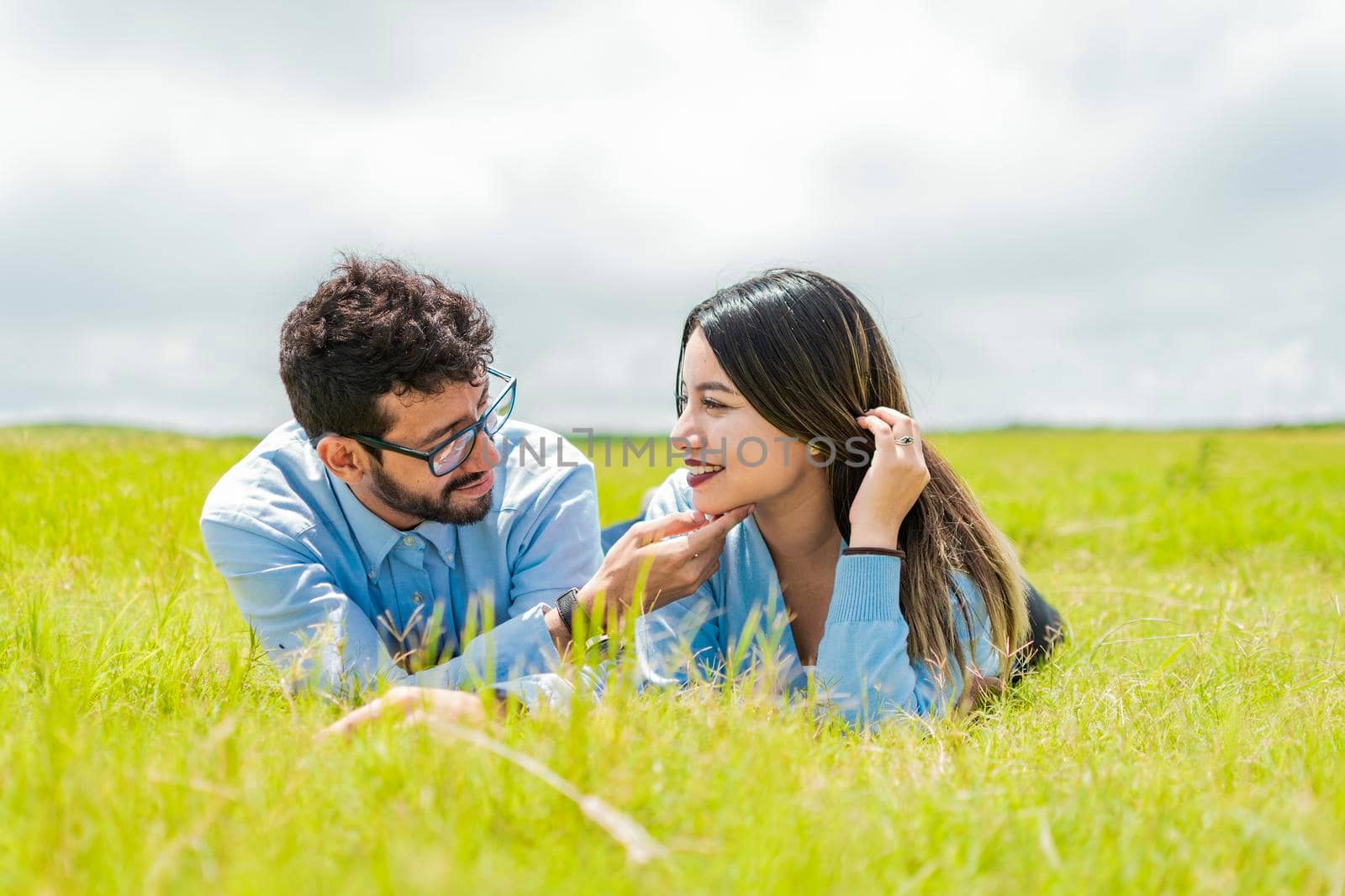 Young couple in love lying on the grass touching each other's faces, two people in love lying on the grass looking at each other, A couple lying on the grass looking at each other