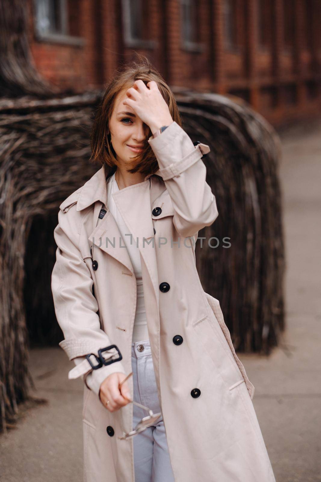 A happy stylish girl in a gray coat walks around the city by Lobachad