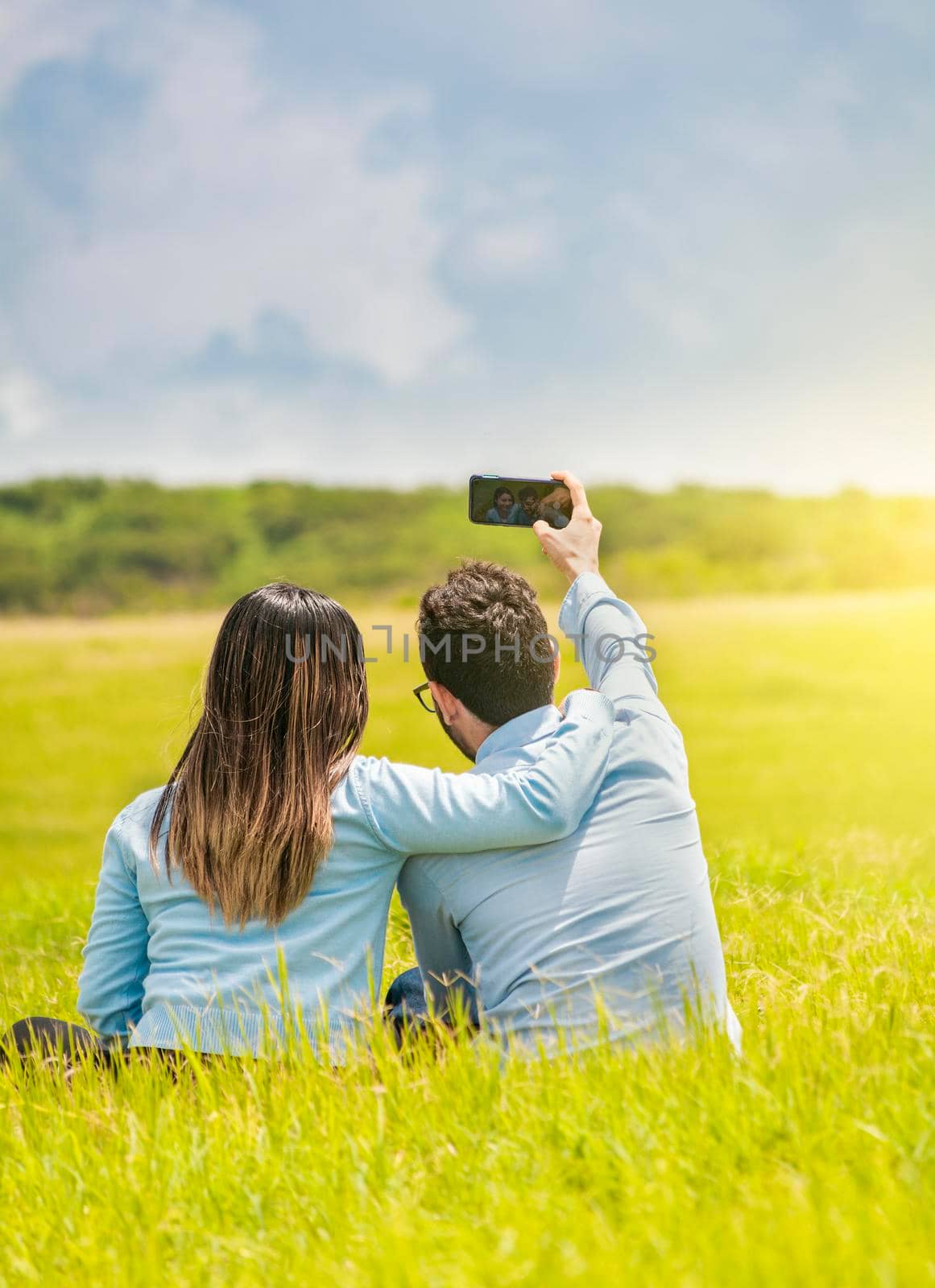 People in love taking selfies in the field with their smartphone, Smiling couple in love sitting on the grass taking selfies, Young couple in love taking a selfie in the field by isaiphoto