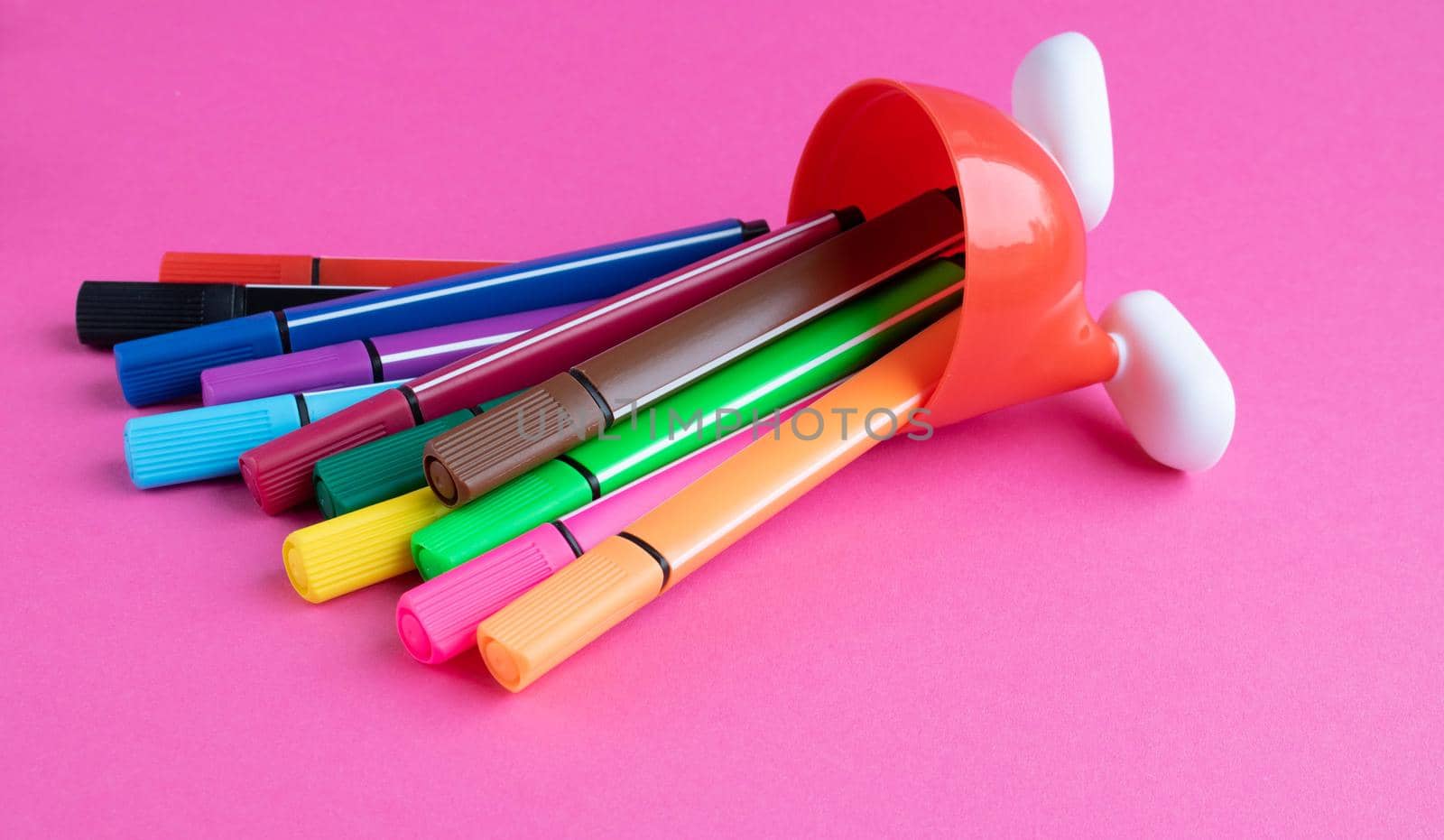 Fallen colored markers and a red stand with white legs isolated on a pink background