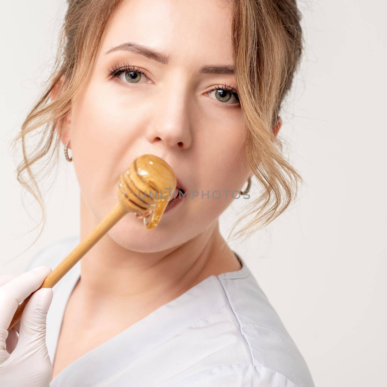 Portrait of beautiful young caucasian woman eating honey with wooden spoon on white background