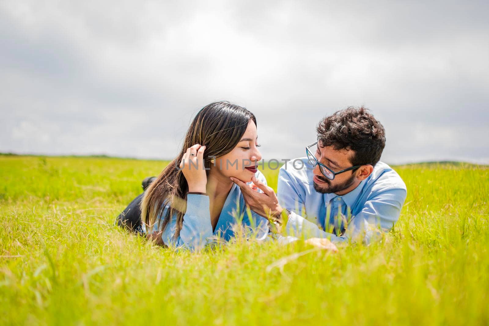 A couple lying on the grass looking at each other, young couple in love lying on the grass touching each other's faces, two people in love lying on the grass looking at each other