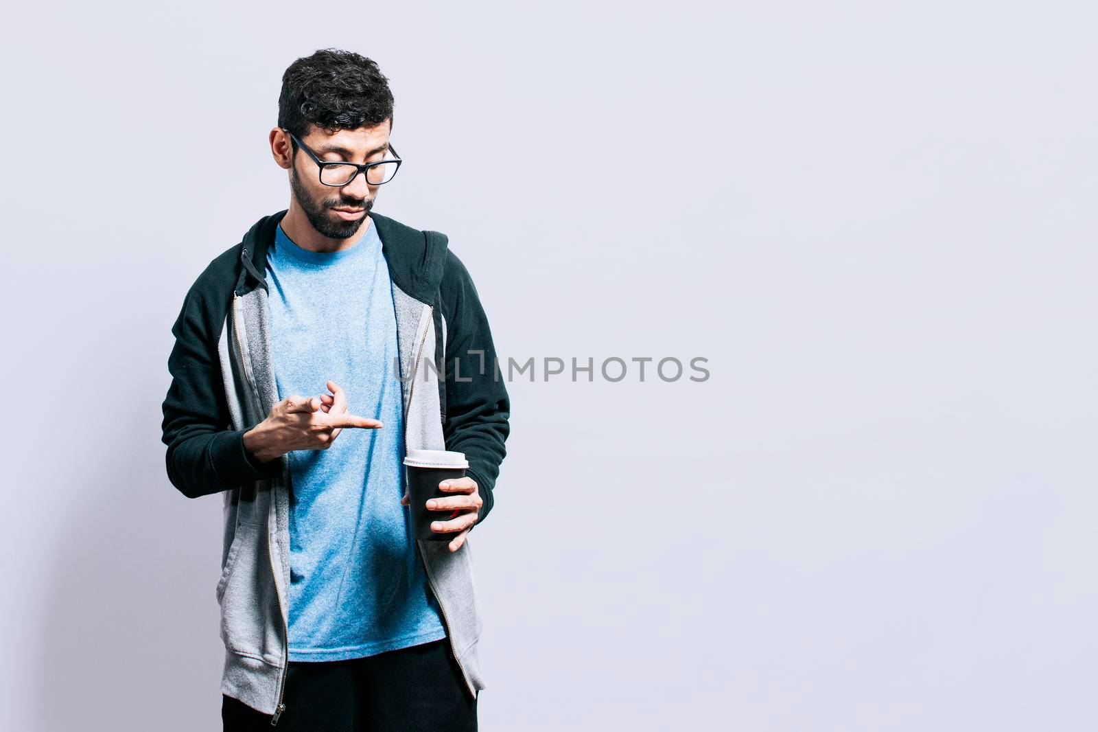 Person with coffee on isolated background, guy pointing disposable cup of coffee on isolated background, concept of a man showing looking at disposable cup of coffee