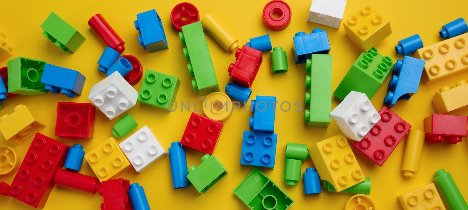 Scattered parts of a plastic children's designer, top view. Yellow background, copy space by ndanko
