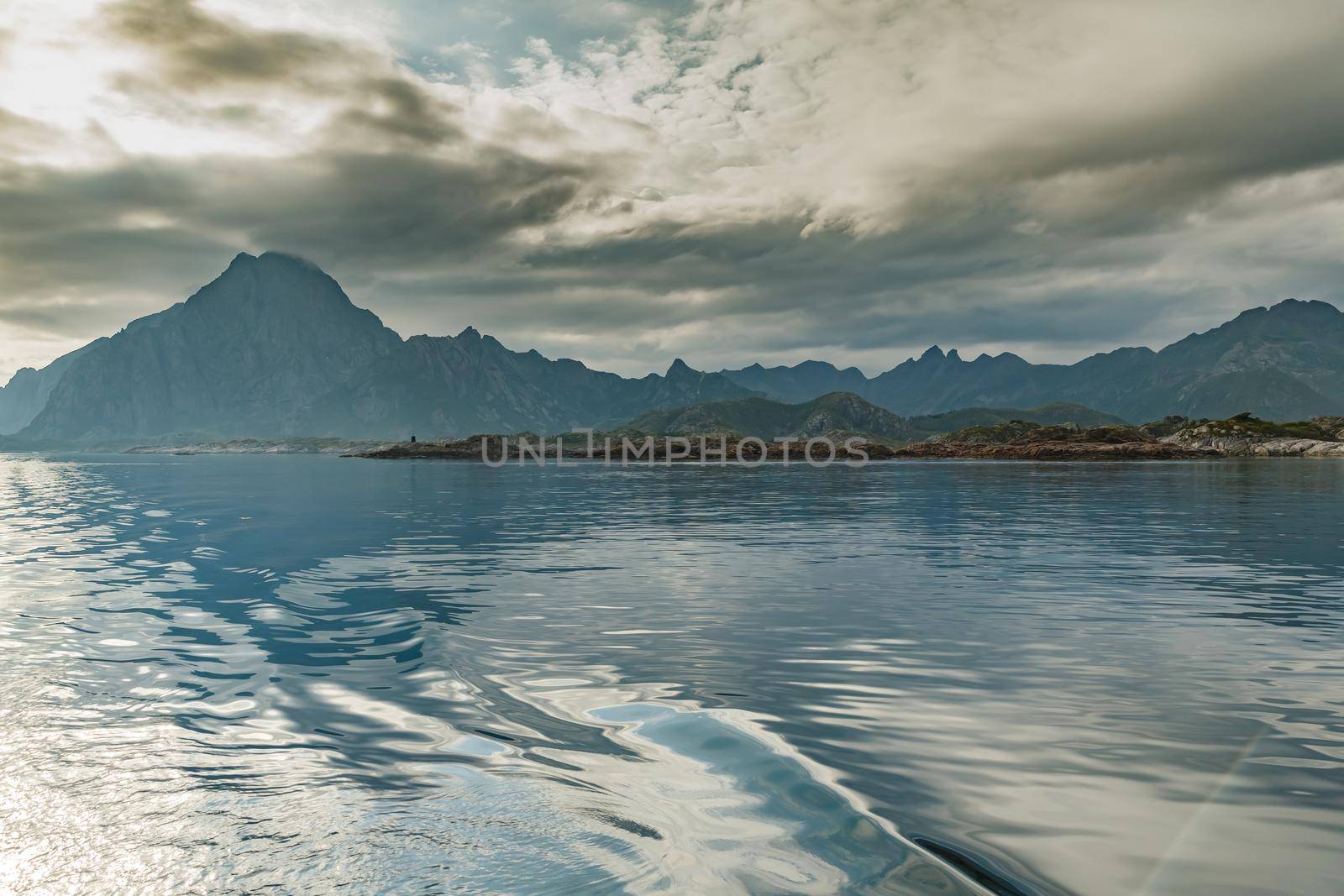 Norwegian seascape, lighthouse on the island, rocky coast with dramatic skies, the sun breaks through the clouds, sheer cliffs, small islands illuminated by the sun. High quality photo