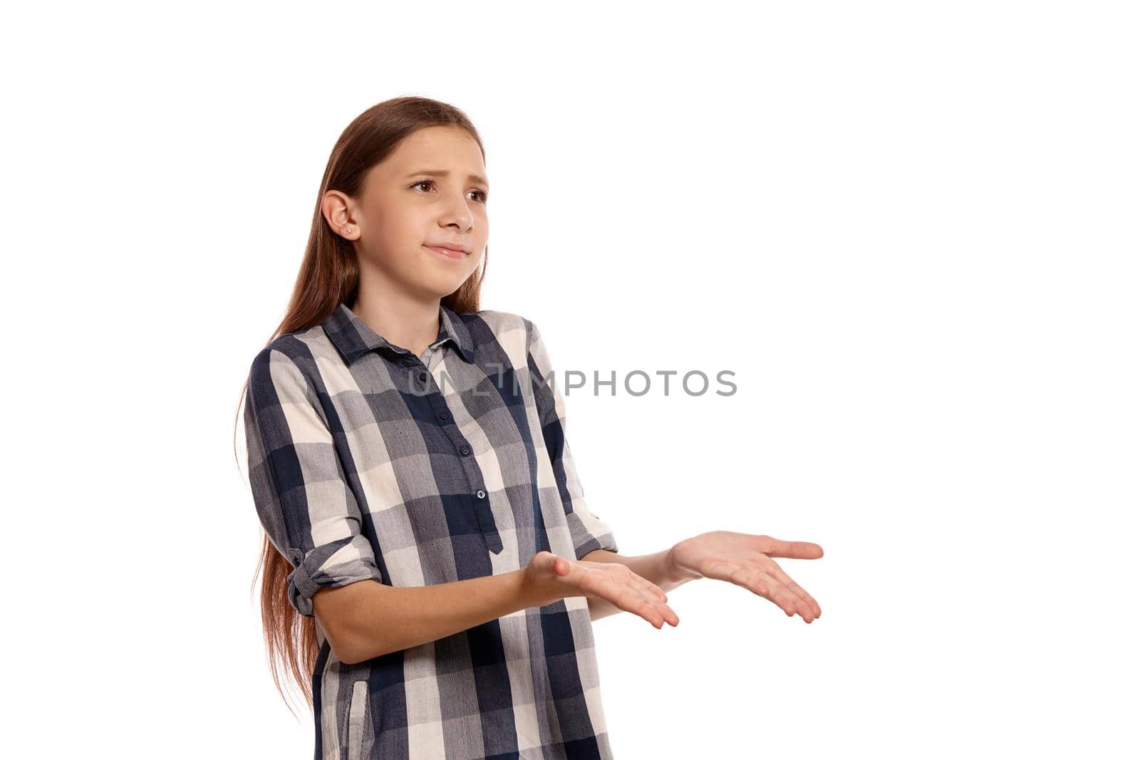 Portrait of a beautiful teenager in a casual checkered shirt looking upset while posing isolated on white studio background. Long hair, healthy clean skin and brown eyes. Sincere emotions concept. Copy space.