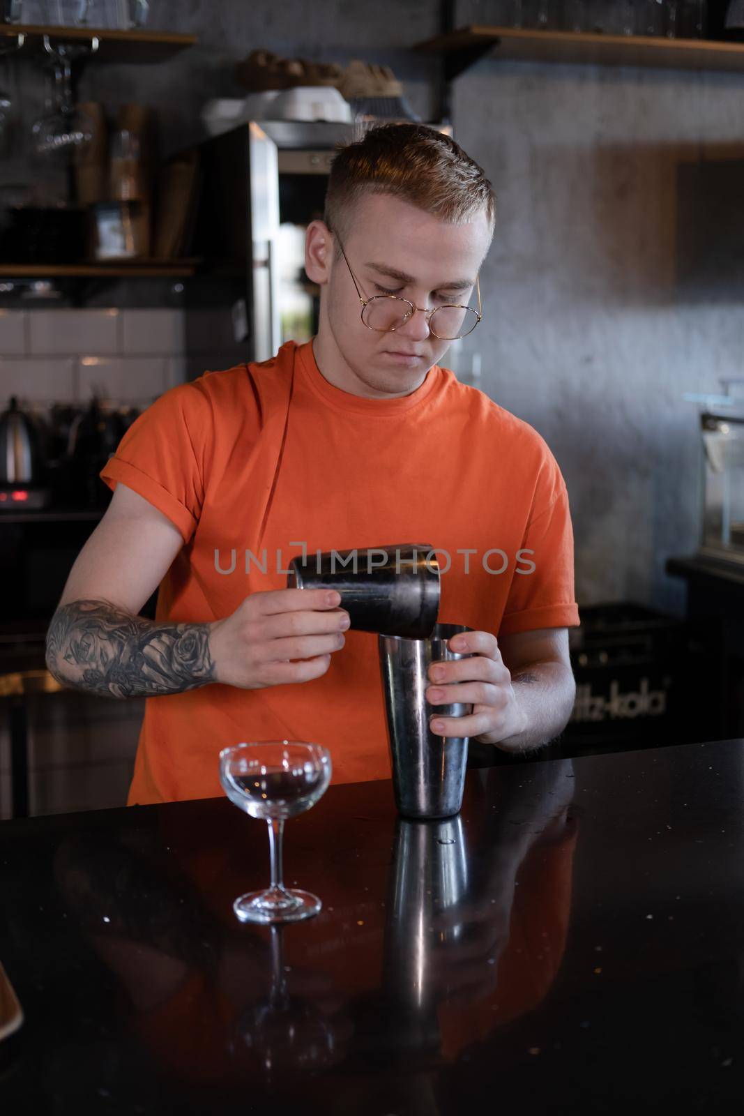 Barman is making cocktail at night club. stylish young man mixing a cocktail in a dark loft cafe. alcohol drink in modern bar. male bartender by oliavesna