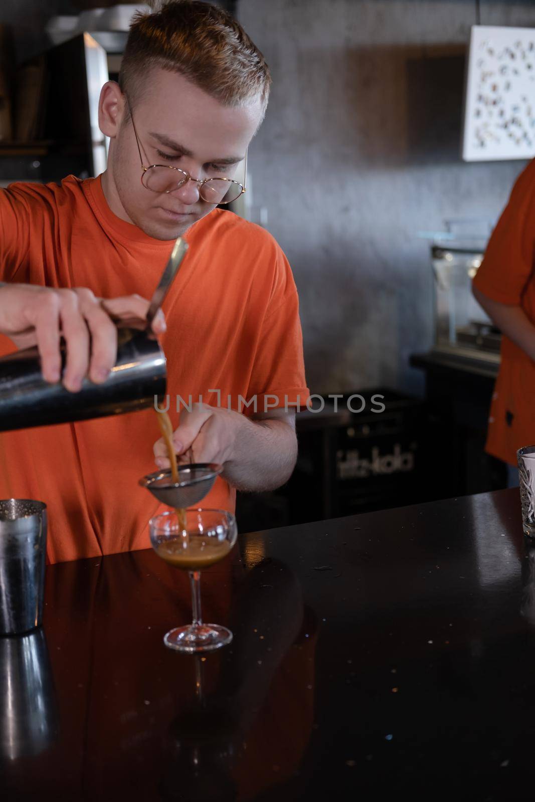 Barman is making cocktail at night club. stylish young man mixing a cocktail in a dark loft cafe. alcohol drink in modern bar. male bartender by oliavesna