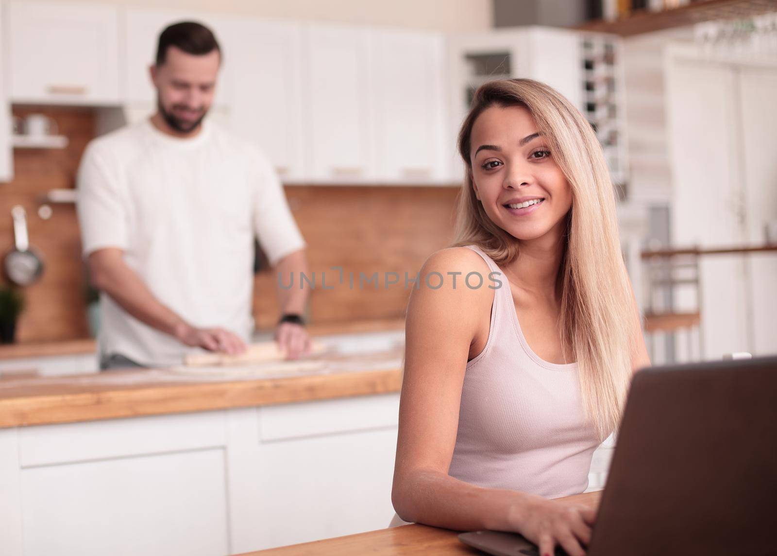 young woman sitting in front of open laptop in kitchen by asdf