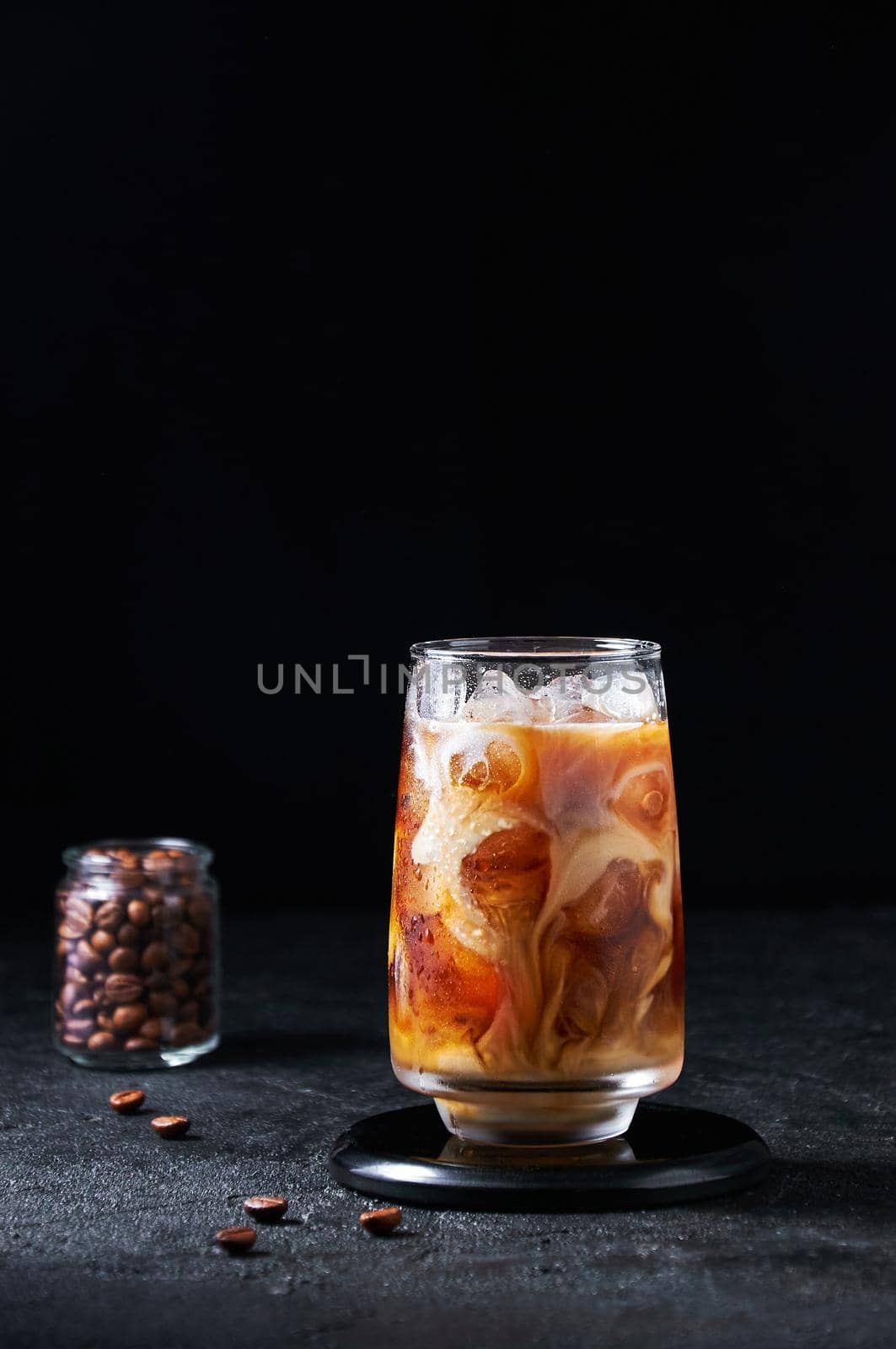 Iced Coffee with Milk in Tall Glass on Dark Background. Concept Refreshing Summer Drink.