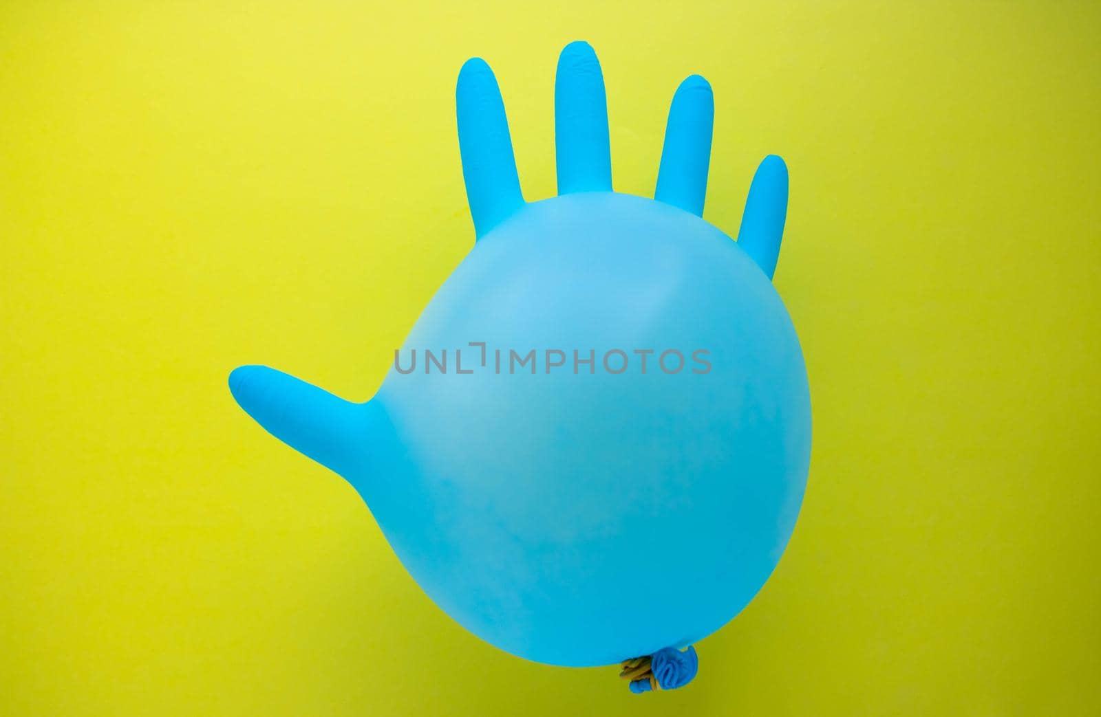 Flying blue rubber surgical glove in the form of a balloon on a yellow background with a copy of space. The concept of minimalism