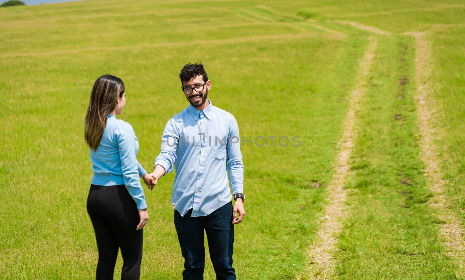 two smiling lovers in the field holding hands, Beautiful couple holding hands looking at each other in the field, two persons holding hands in the field