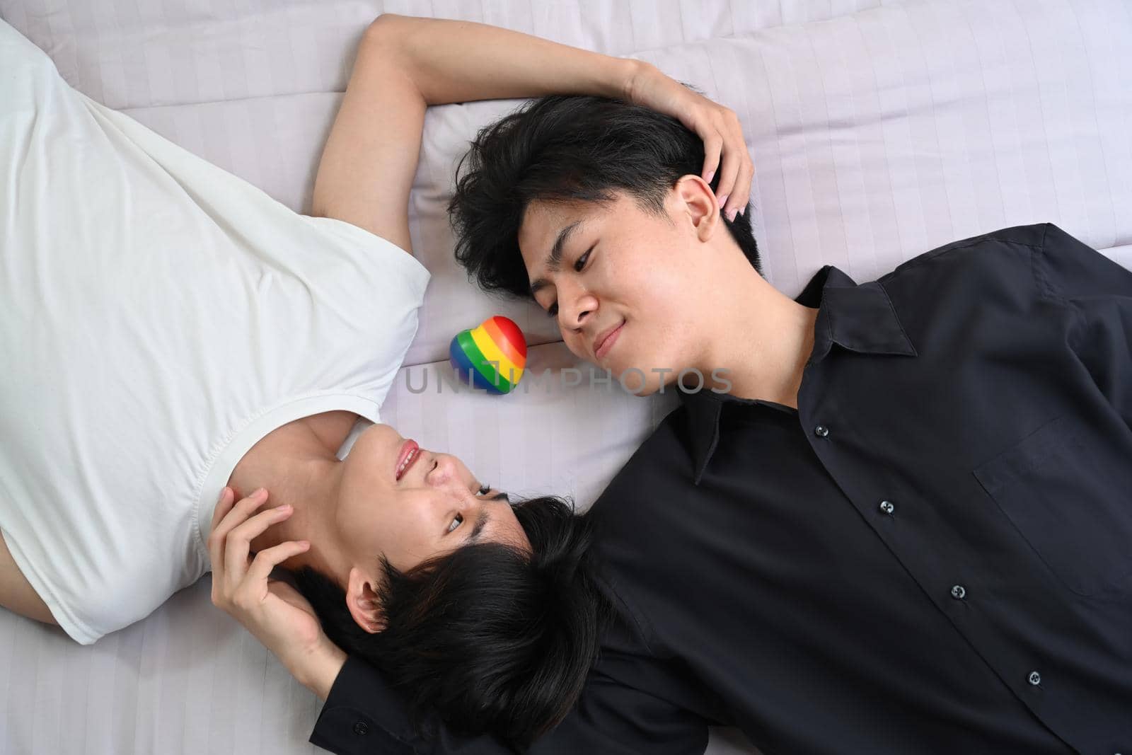 Happy homosexual couple lying down on bed, spending time together at home. Concept of sexual freedom and equal rights for LGBT community by prathanchorruangsak