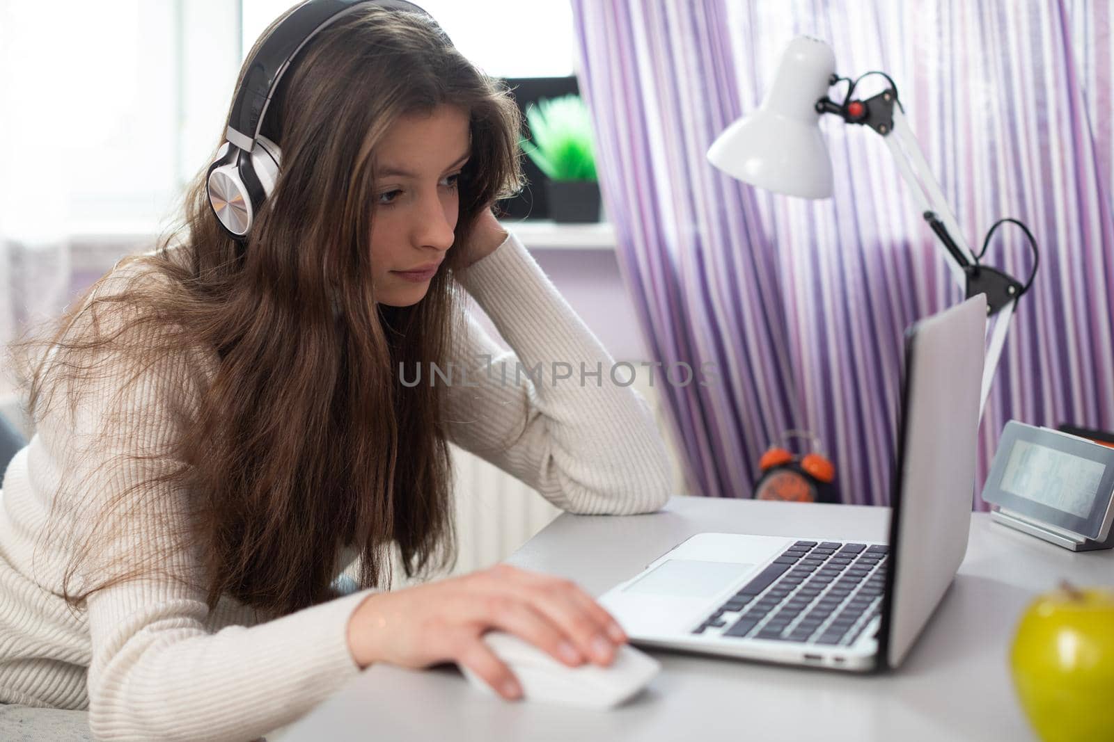 A young female student is taking schoolwork via the internet. An attractive brunette with long hair sits at a desk near a window.