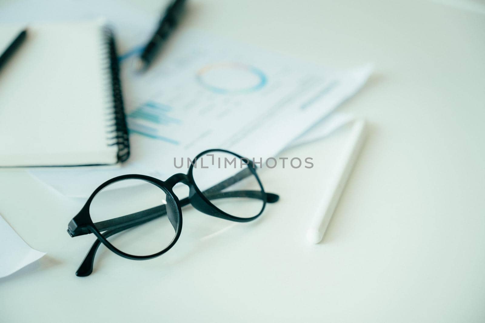 Close up image of black eyeglasses with document graph, notebook, stylus pen on the table Business concept.