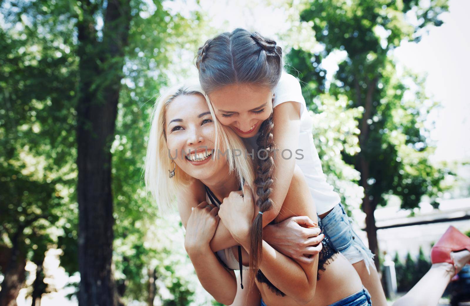 Young woman riding piggyback on friend by Novic