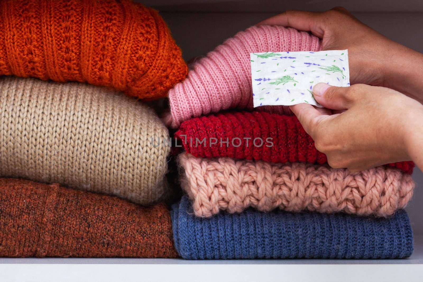 Cropped woman hands putting sachet with dried lavender between cloth in stack on shelf in wardrobe
