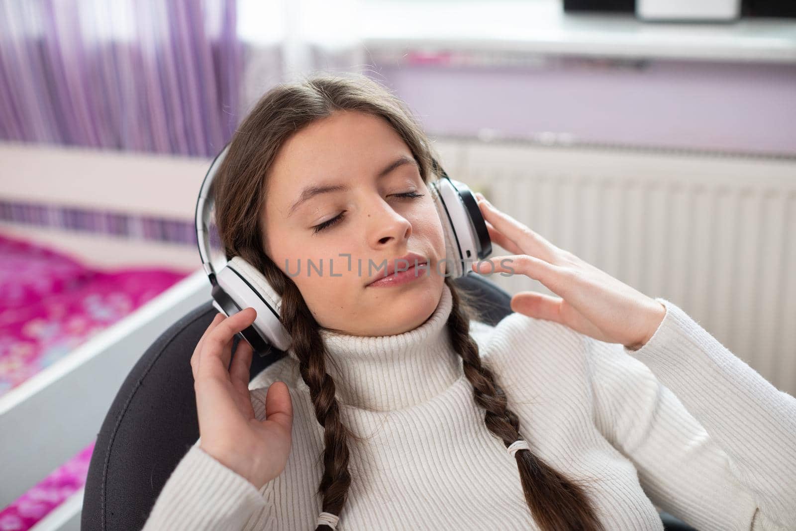 Close-up frame of a young brunette woman listening to music on wireless headphones. Closed eyes. Pretty girl with braids and glasses.
