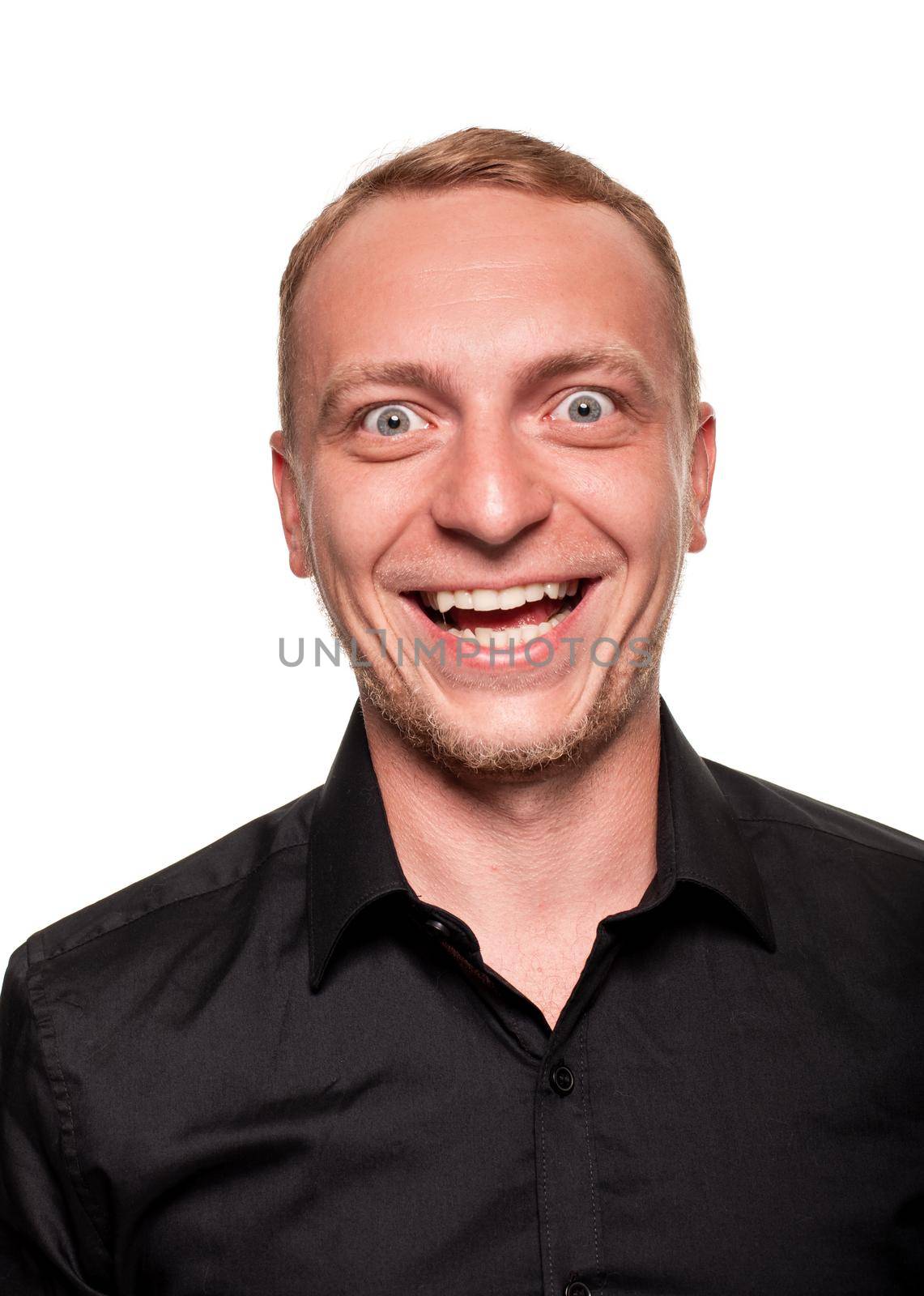 Handsome young blond man in a black shirt is making faces, smiling and staring into the camera, isolated on a white background