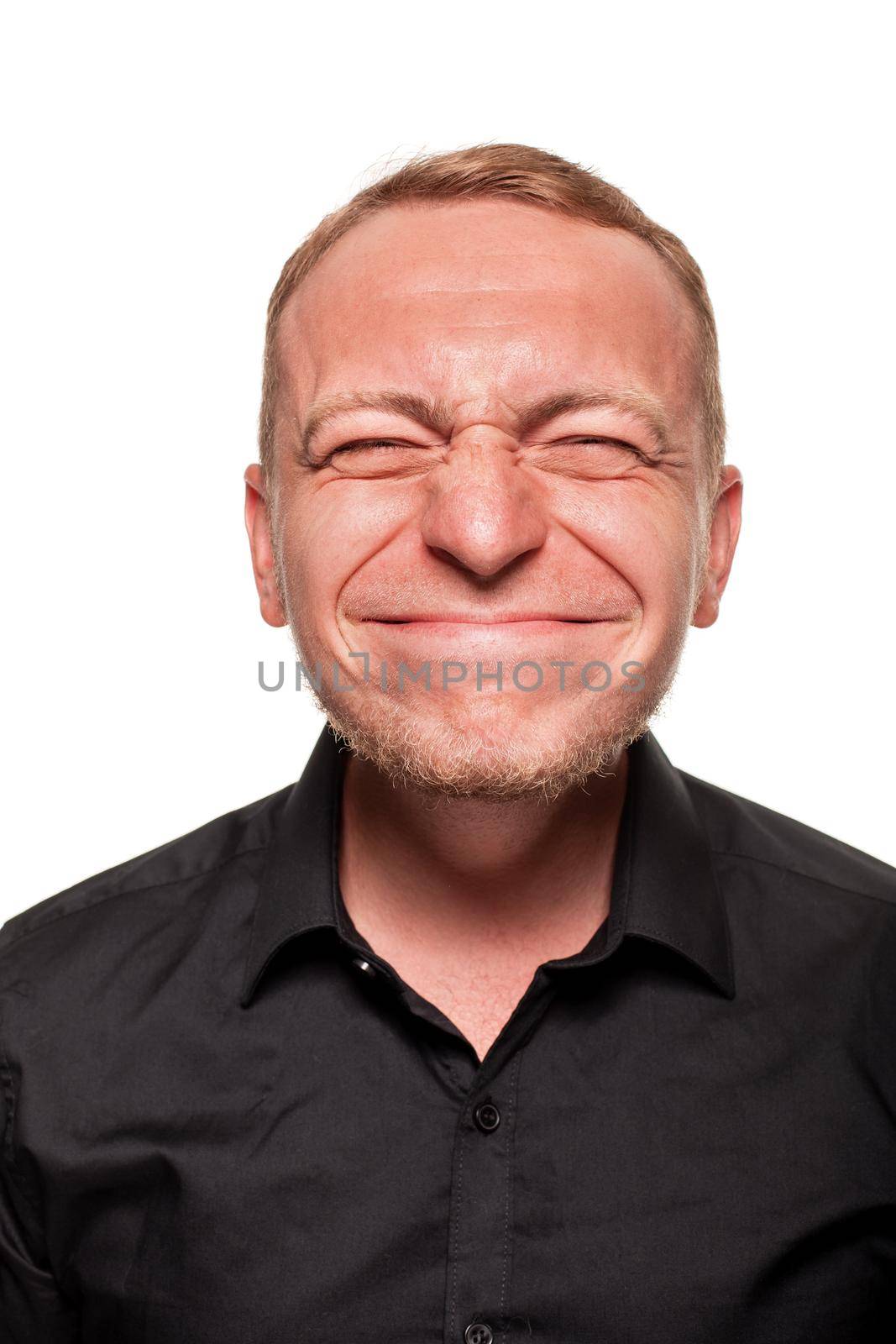 Handsome young blond man in a black shirt is making faces at the camera, isolated on a white background