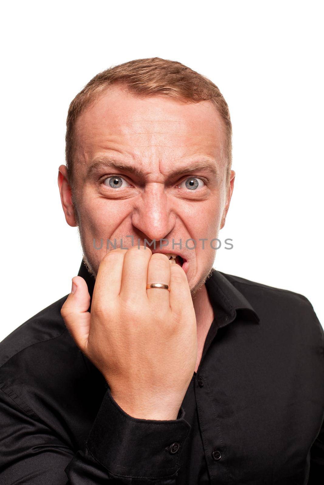 Handsome young blond man in a black shirt is making faces and act like he is biting his nails, isolated on a white background