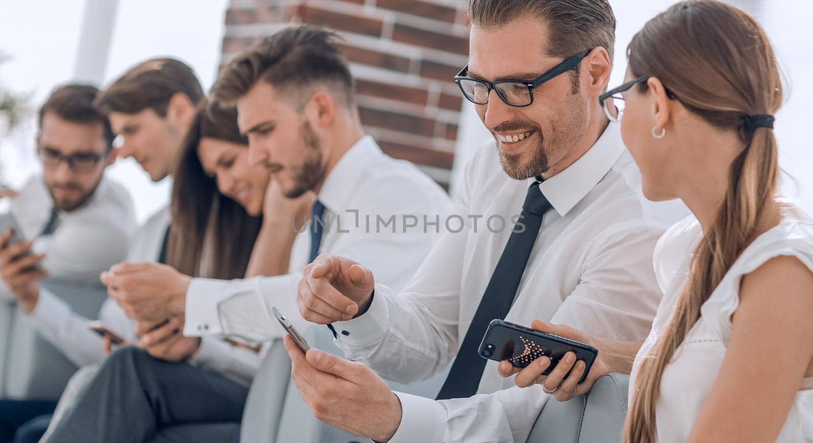 employees of the company using their smartphones sitting in the office lobby by asdf