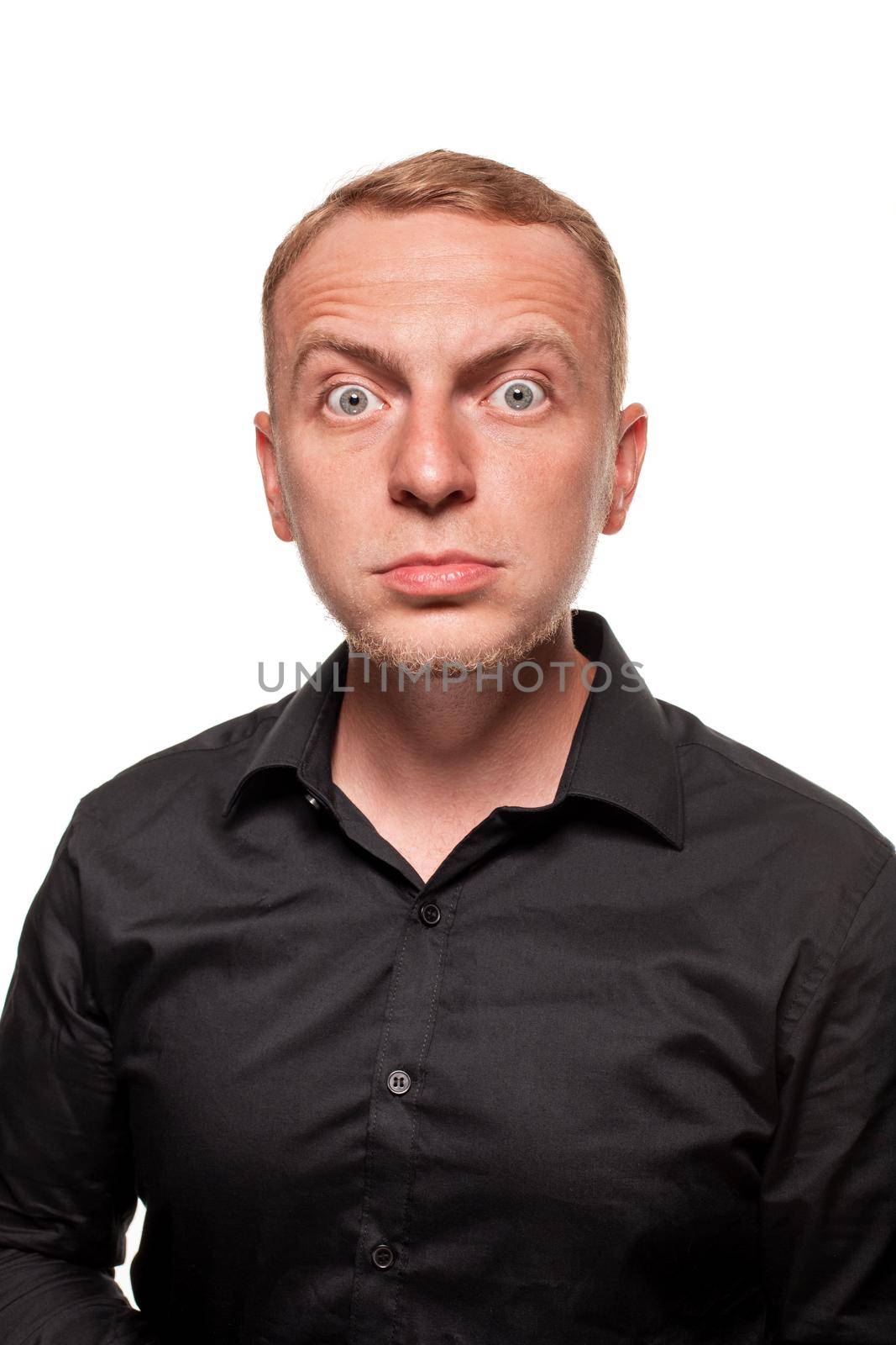 Handsome young blond man in a black shirt is making faces and staring at the camera, isolated on a white background