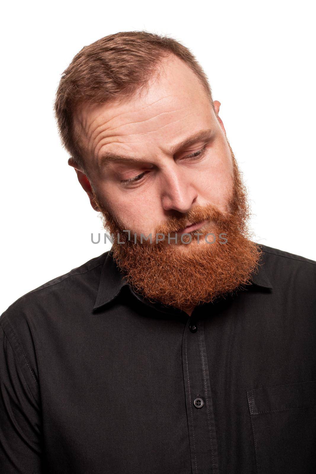 Portrait of a young, redheaded man with a beard in a black shirt, looking down and wondered, isolated on a white background