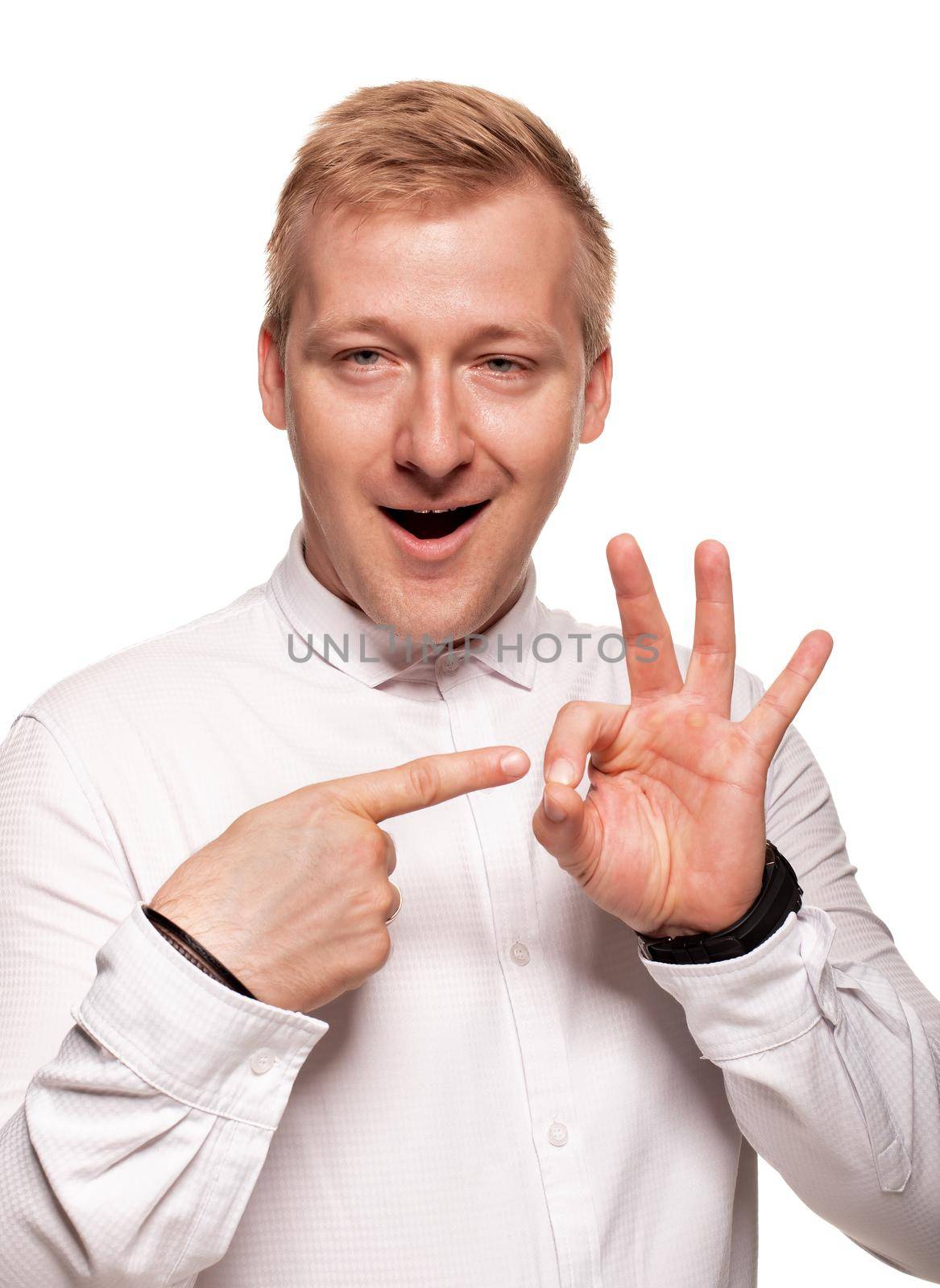 Imposing, young, blond man in a white shirt, with black watches is gesticulating and smiling, while standing isolated on a white background