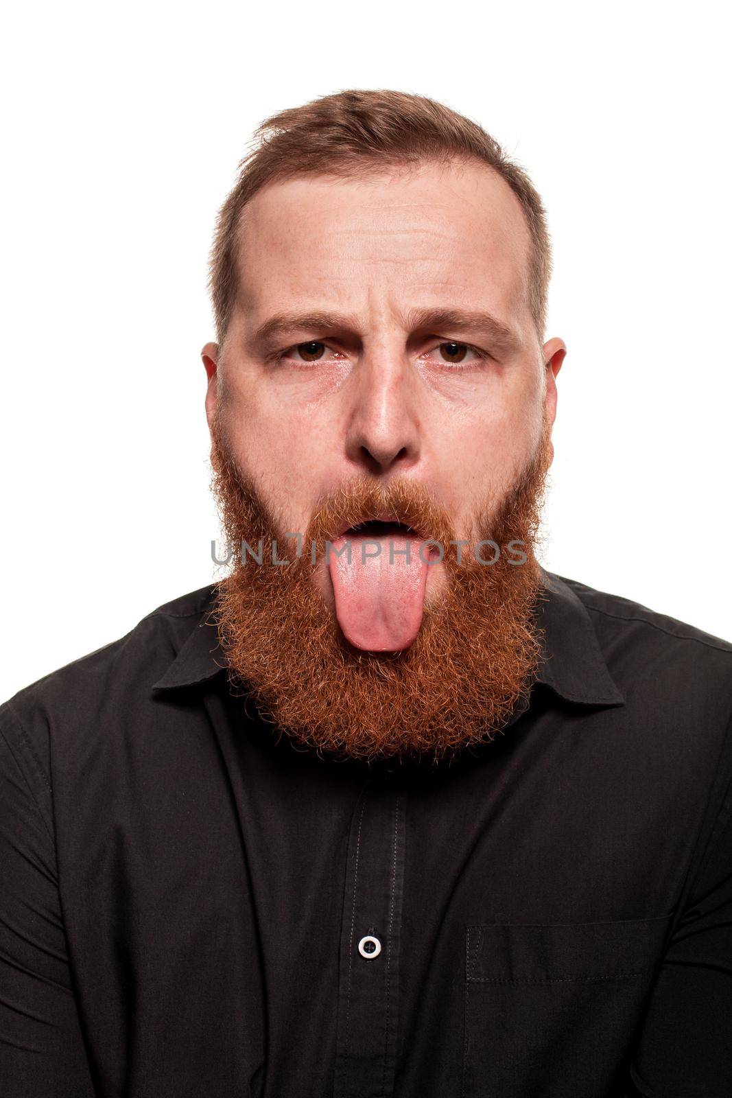 Portrait of a young, chubby, redheaded man with a beard in a black shirt, showing his tongue at the camera, isolated on a white background