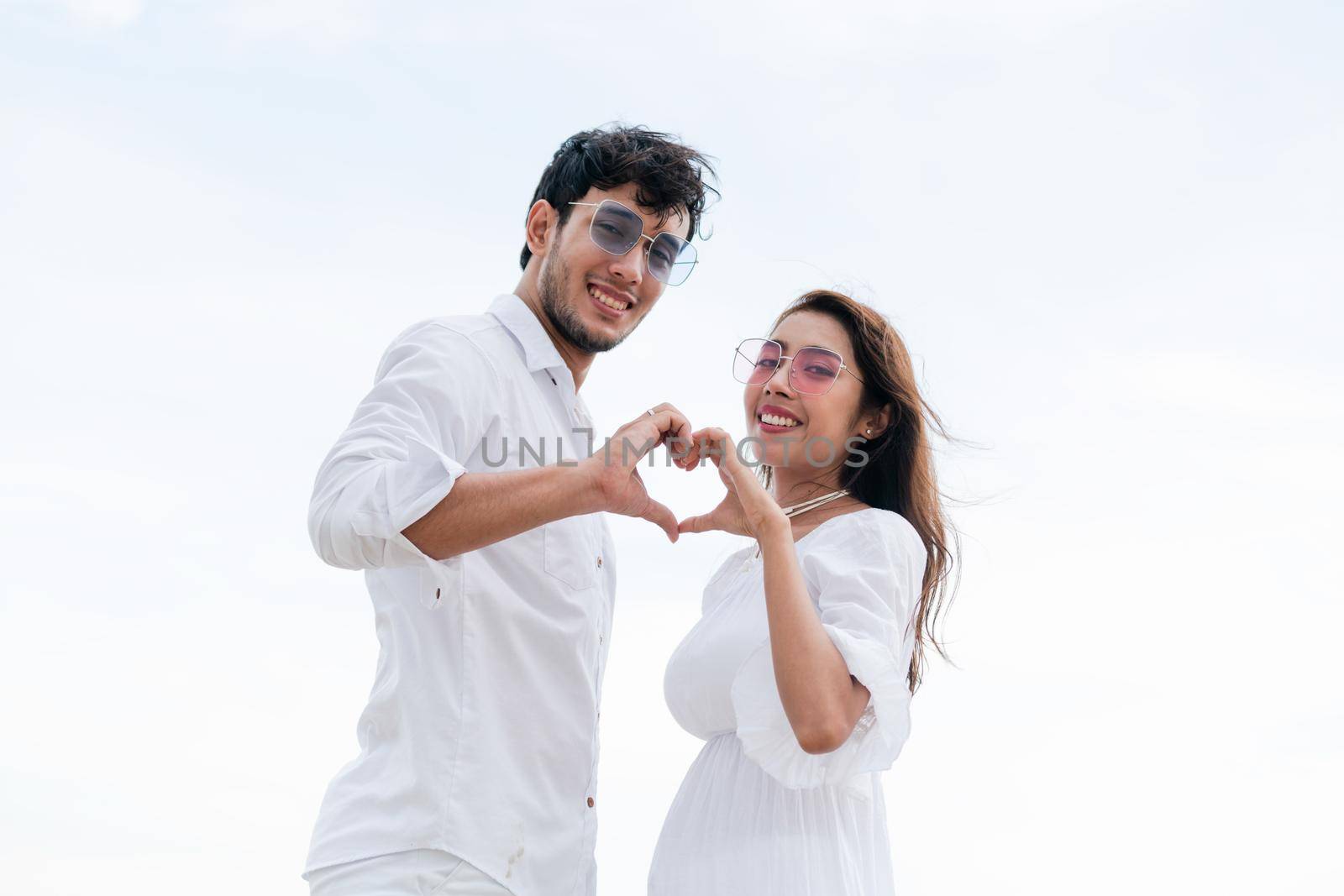 Young couple shows heart shape hand gesture on the beach in summer.