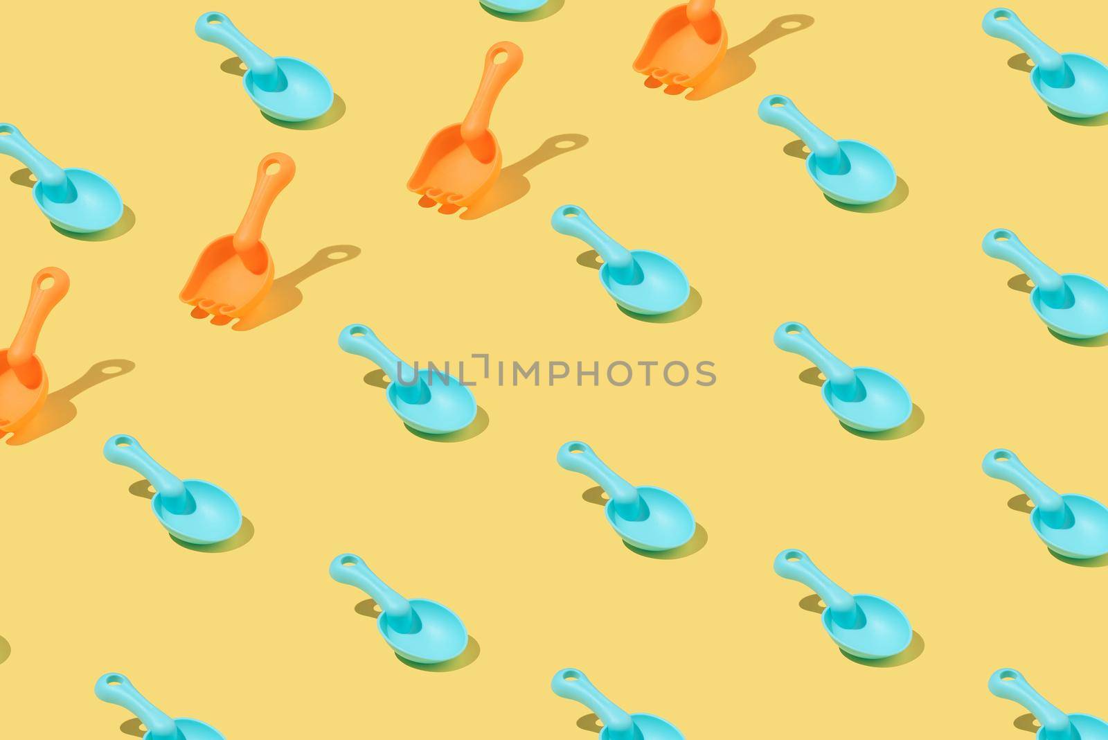 Creative pattern made of blue and orange plastic beach toy shovels isolated on yellow background. Rectangle layout. Isometric.