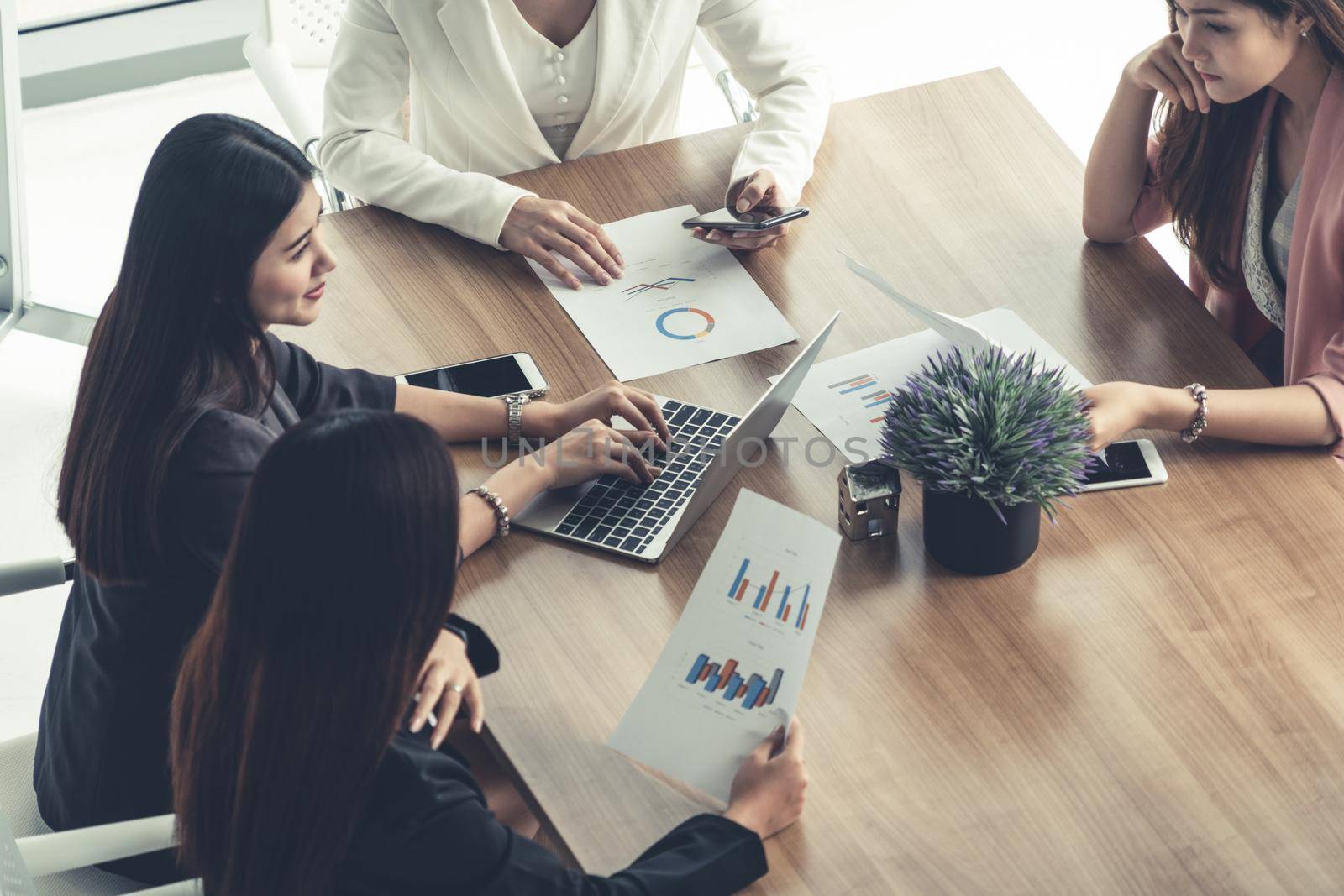 Businesswoman in group meeting discussion with other businesswomen colleagues in modern workplace office with laptop computer and documents on table. People corporate business working team concept.