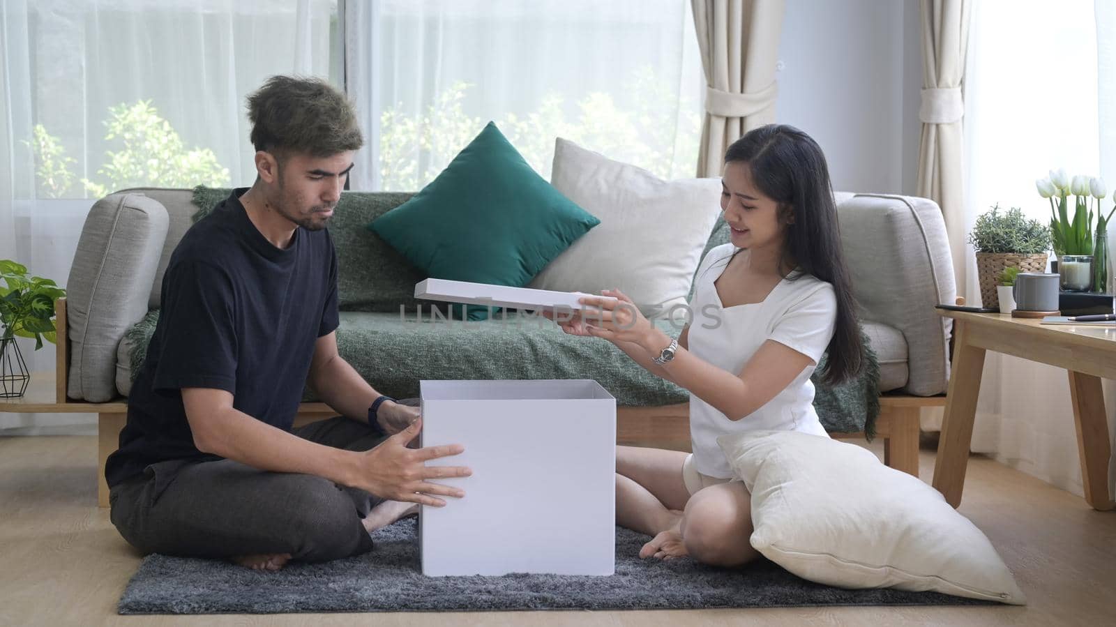 Young asian couple sitting in floor and unpacking cardboard boxes at new home. Relocation house renovation, removals concept.