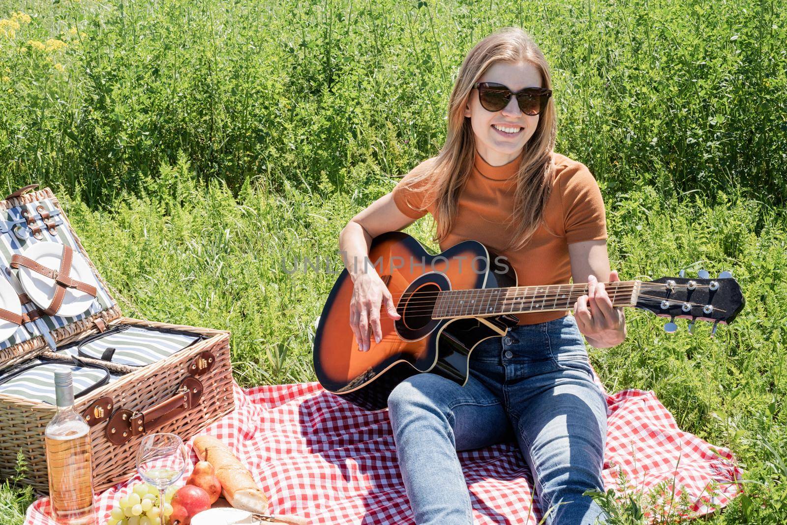 millennial woman in summer clothes and sunglasses playing guitar on a picnic