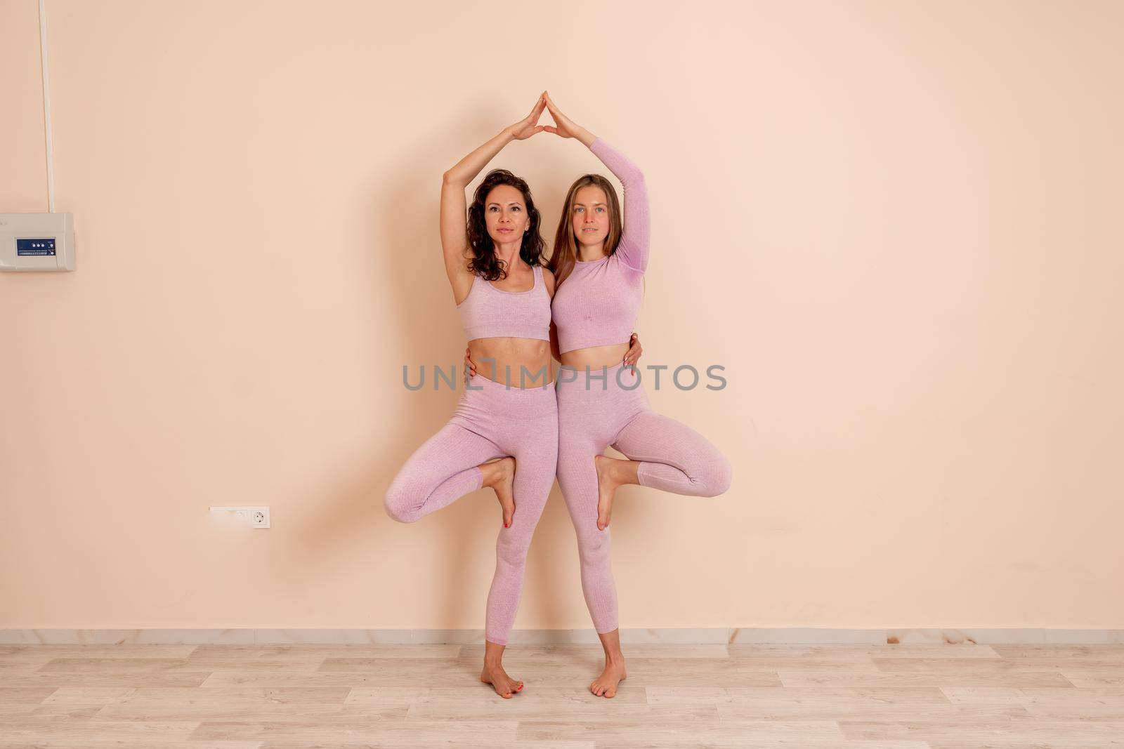 Two beautiful women cook doing yoga, sports together in the gym. Dressed in pink suits. The concept of grace and beauty of the body