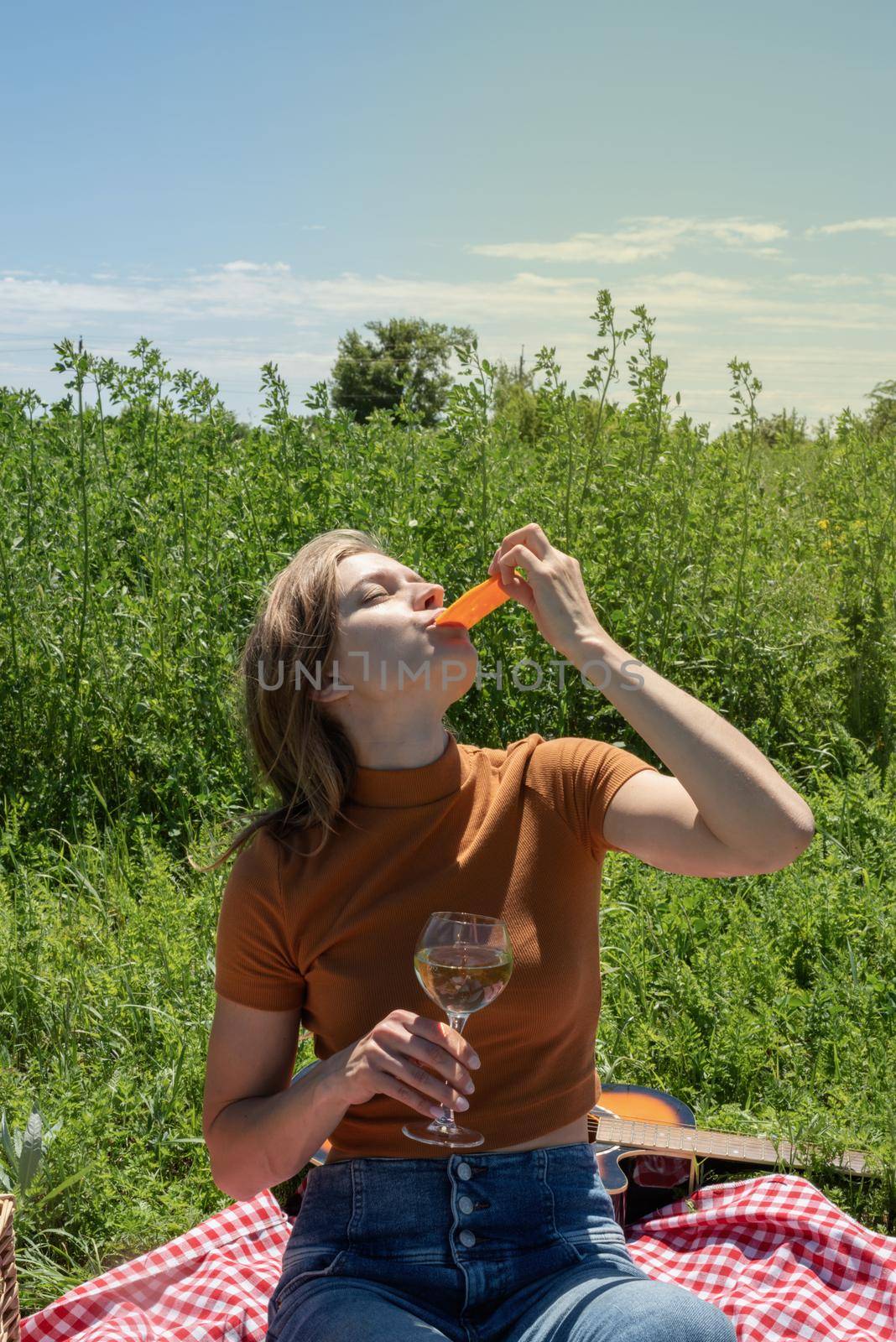 Young woman in park outside at sunny day, enjoying summertime dreaming and drinking wine. Millennial woman having picnic outdoors in sunny day