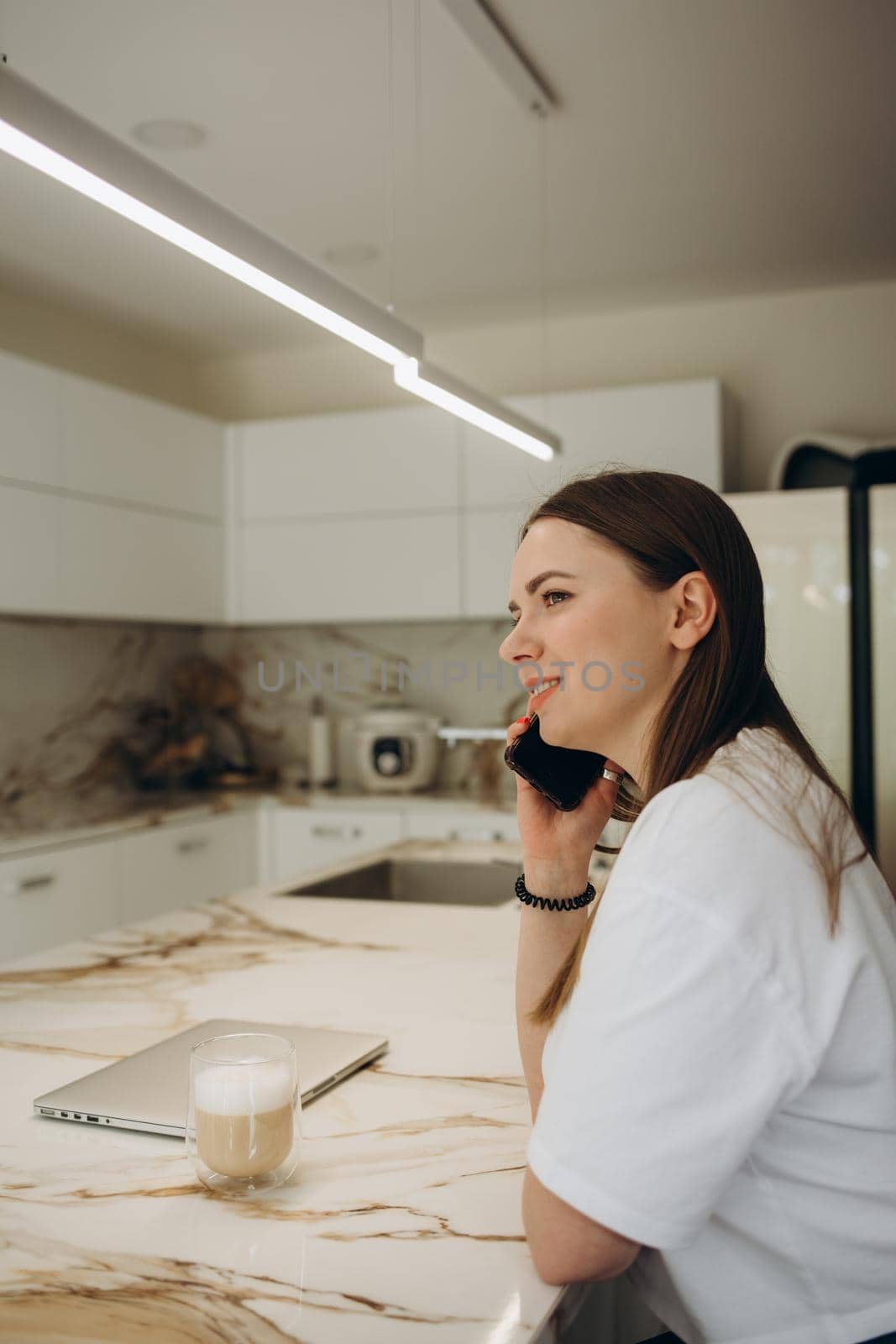 Happy Woman Talking On Mobile Phone While Cooking In Kitchen.