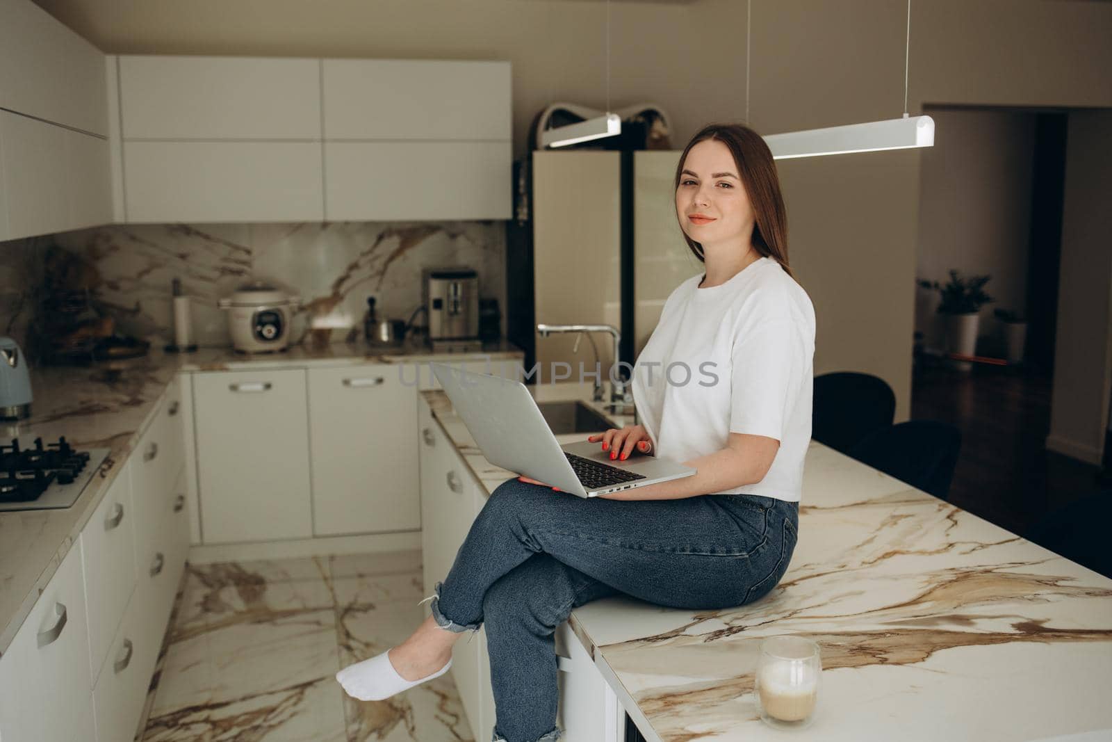 Attractive young woman working on laptop while sitting in the kitchen at home by fentonroma
