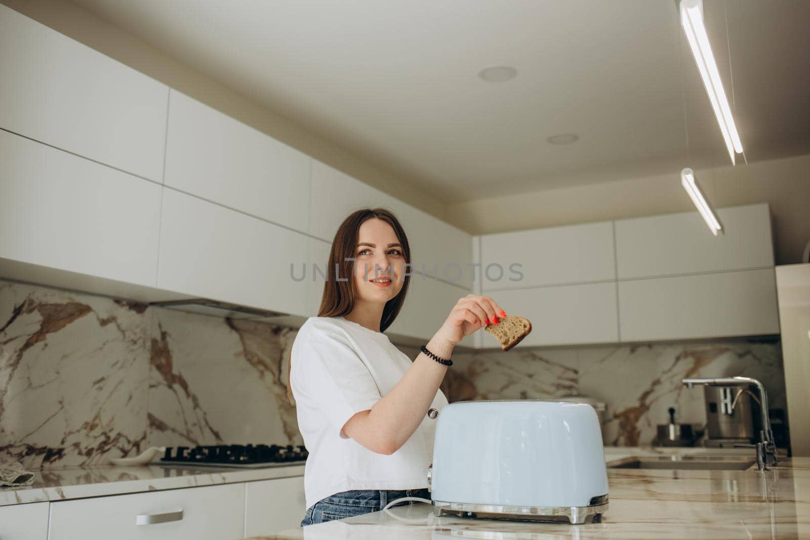 Pretty young woman preparing a toast at home in the kitchen. Modern interior, furniture for the kitchen. Cook at home. Healthy eating and diet