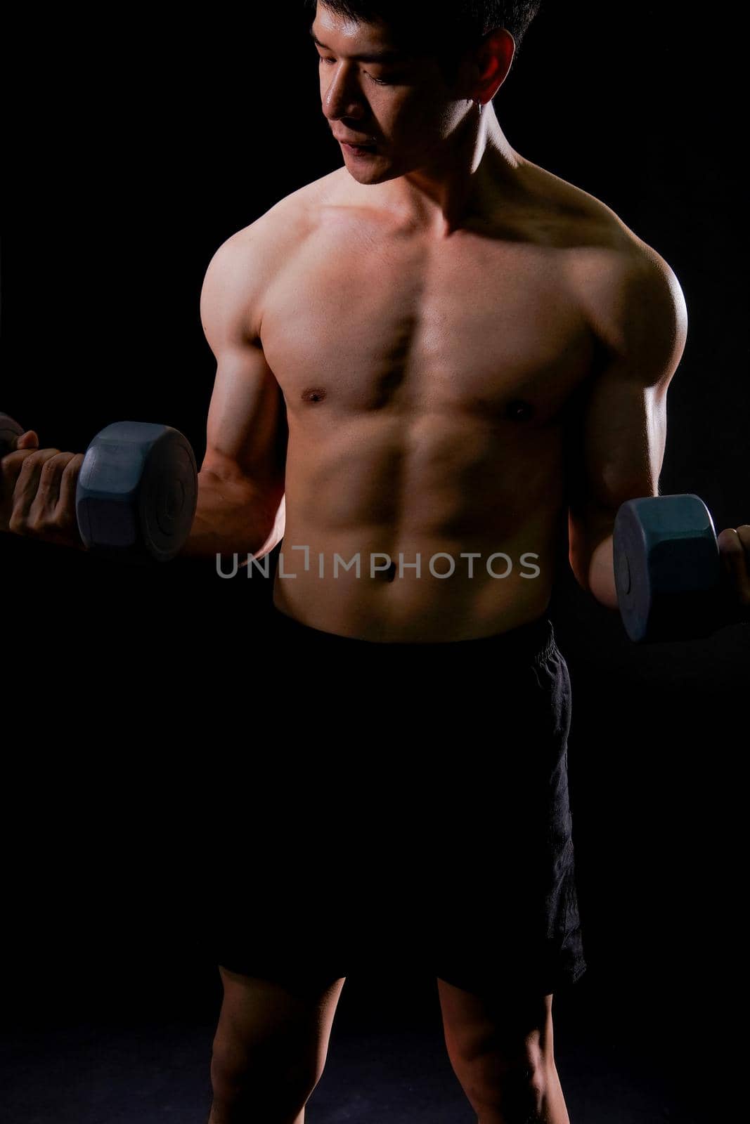 portrait of athletic muscular bodybuilder man with naked torso six pack abs working out with dumbbell. fitness sport exercise concept