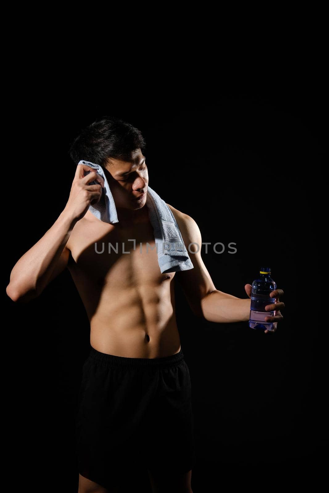 portrait of athletic muscular bodybuilder man with naked torso six pack abs holding water bottle. fitness workout concept