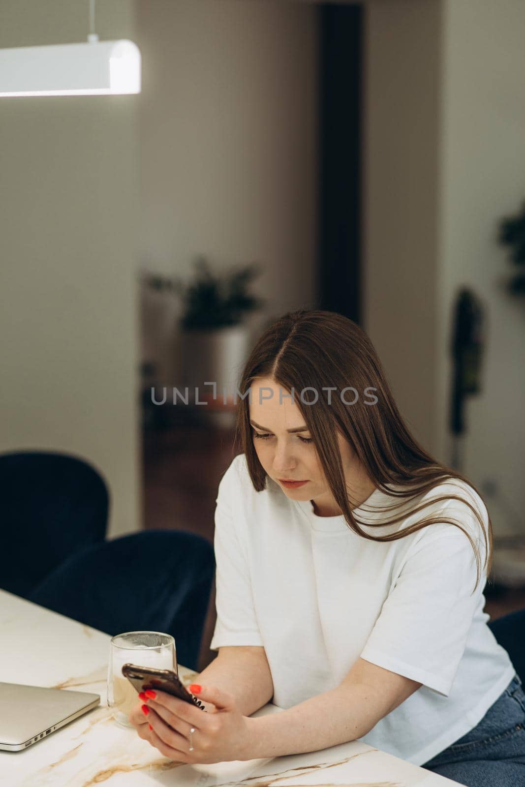 Beautiful woman drinking coffee and using the phone in the kitchen. Young woman enjoying in morning